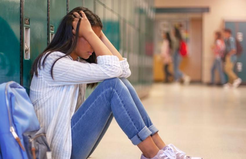 Student sitting alone in a school hallway, highlighting youth mental health challenges.
